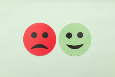 Açık yeşil arka planda kırmızı üzgün ve yeşil gülen surat ifadeleri. İkili geri bildirim, müşteri memnuniyeti derecesi, artılar ve eksiler ve zihinsel sağlık değerlendirmesi kavramı. Minimalist düzlük.