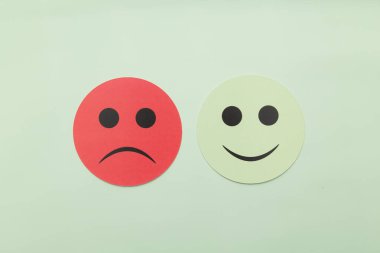 Yeşil arka planda mutlu ve üzgün duyguları gösteren iki kağıt surat. Müşteri geribildirimi, memnuniyet derecesi, artılar ve eksiler ve zihinsel sağlık değerlendirmesi kavramı. Minimalist düzlük.