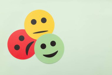 Yeşil arka planda üzgün, tarafsız ve mutlu yüzlü kağıt simgeler. Müşteri memnuniyeti anketi, iş görüşmeleri, değerlendirmeler ve akıl sağlığı konsepti. Minimalist üst görünüm.