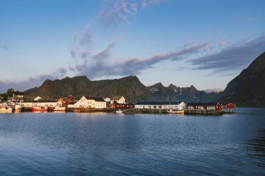 Norveç, Lofoten takımadalarında gün doğumunda Reine balıkçı köyü ve arka planda dağlar üzerinde güzel renkli bir gün doğumu.. 