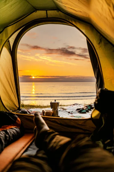 Camping with tent in Lofoten islands, Northern Norway, Kvalvika beach, during sunset. Person sitting in the tent.