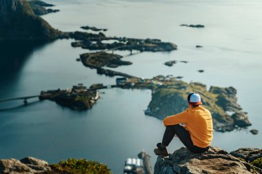 Norveç 'te uzun bir yürüyüşten sonra bir dağın zirvesinde oturan turuncu tepeli erkek, Lofoten