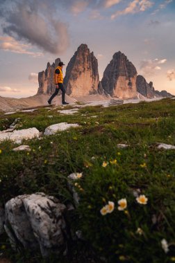 Gün batımında Tre Cime di Lavaredo 'nun üç tepesinde çiçek arkaplanı ve arka planda yürüyen bir erkek.