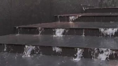 Şehirde şiddetli yağmur. Su merdivenler boyunca akar ve siyah taş duvar.
