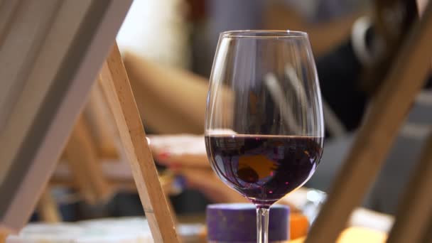 Un bicchiere di vino a un master class di pittura. Le mani femminili nello sfondo dipingono un quadro. — Video Stock