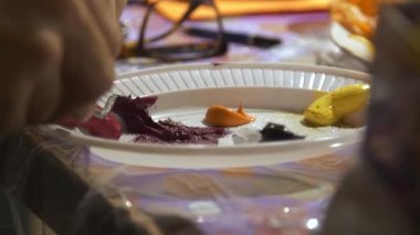 Palet bıçaklı bir el, sehpa olarak kullanılan beyaz plastik plakadan yağ boyası alıyor..