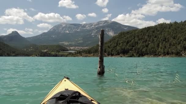 Kayak en un lago esmeralda con fondo de montaña. Un kayak amarillo pasa por un viejo tronco de árbol. — Vídeo de stock