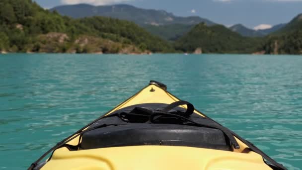 Een gele kajak slingert langzaam op een smaragd meer met berg en lucht achtergrond. Reisconcept. — Stockvideo