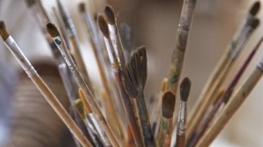 Arka planda bir kişinin olduğu bir tencerede bir grup kuru sanatsal boya fırçası. Sanat okulu kavramı.