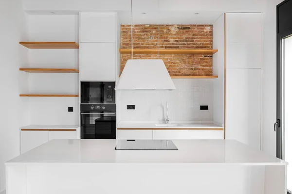Modern eingerichtete Loft-Wohnung mit weißer Inselküche, großer Arbeitsplatte, Holzregalen und Ziegelmauer — Stockfoto