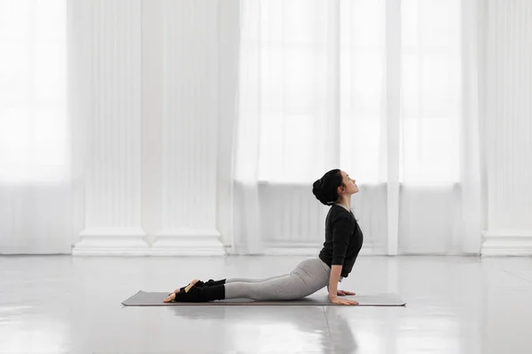 Cobra Pose. Krásná mladá asijka cvičení jóga póza na šedé podložce v jóga studio. — Stock fotografie