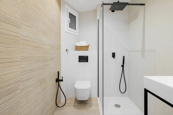 Interieur van moderne stijl badkamer in witte en beige kleuren in gerenoveerd appartement. Doucheruimte en toilet, met zwarte kranen, handdoeken en betegelde vloer en muren. Rechtenvrije Stockfoto's