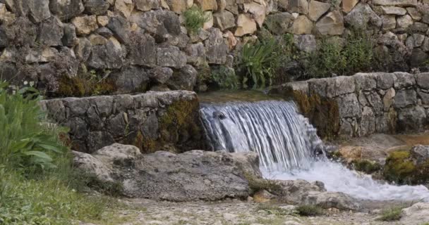 Corriente de agua fría de montaña fluye a través de la zona rural en un día soleado con mampostería de piedra alrededor. — Vídeos de Stock