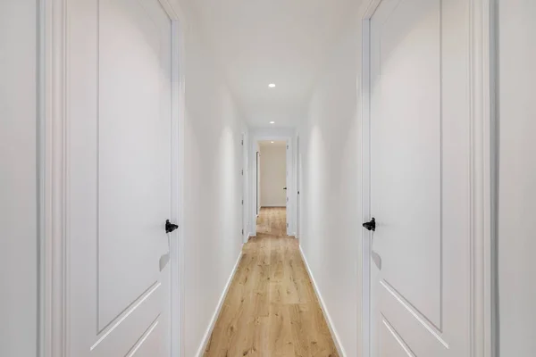 Interior of long narrow hallway with closed doors, wooden floor and white walls in apartment designed in minimal style — Stock Photo, Image