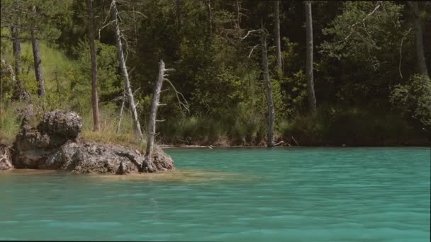 Vista do barco nadando lentamente até a margem do lago esmeralda. Água de lago azul com árvores verdes ao redor. — Vídeo de Stock