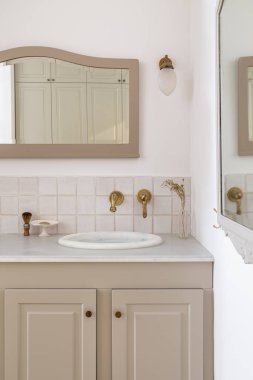 Lavabo, altın musluk ve klasik aynayla bej renkte dekore edilmiş banyo. Eski ya da klasik tarzda tuvaletin içi.