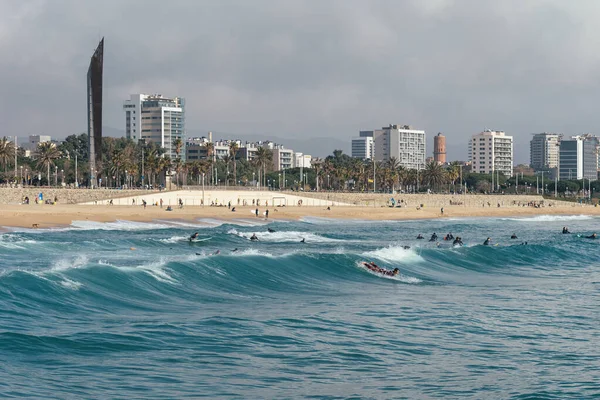 Many surfers at blue sea waves on beach with the background of Barcelona city on sunny day. Rechtenvrije Stockafbeeldingen