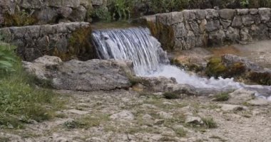 Güneşli bir günde kırsal bölgede küçük bir dağ nehri şelalesi taştan duvarlarla çevrili..