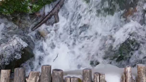 Bovenaanzicht op oude houten brug over de wilde bergrivier in de winter. Water stroomt door bevroren stenen met ijs en mos. — Stockvideo