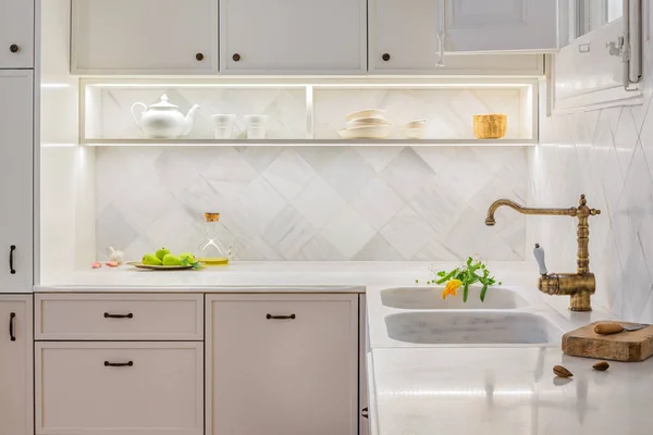 Stijlvolle keuken met accessoires. Helder beige interieur met verlichte planken en verse groenten op tafelblad. Ingericht in vintage stijl. Rechtenvrije Stockfoto's