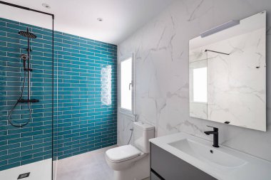 Koyu akuamarin ve beyaz renklerle süslenmiş. Duş bölgesi, yeni lavabo ve tuvaleti olan modern fayanslı banyo..