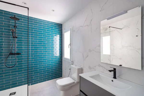 Décoré avec un aquamarin foncé et des couleurs blanches. Salle de bains moderne carrelée avec zone de douche, lavabo neuf et toilettes. — Photo