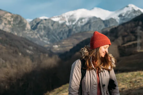 Портрет улыбающегося путешественника на фоне снежных гор. Счастливая женщина в красной кепке, согревается и наслаждается солнечным светом во время похода в горы. — стоковое фото