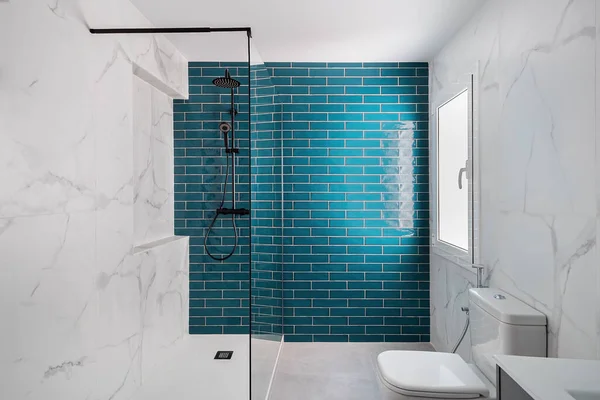 Sötét akvamarinnal és fehér színekkel díszítve. Modern csempézett fürdőszoba zuhanyzóval, új mosdó és WC. Stock Kép