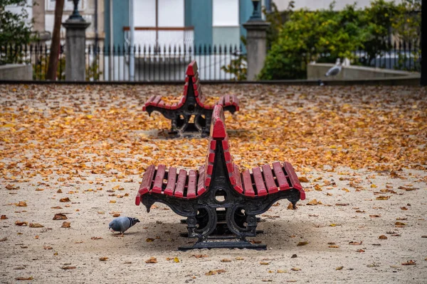 Empty old red benches in city autumn park with fallen leaves. — Stock Photo, Image