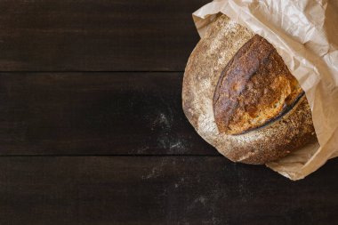 Koyu ahşap zemin üzerinde ev yapımı buğday ekmeği ve un parçaları. Fırında pişmiş ekmek yüzey dokusunun üst görüntüsü