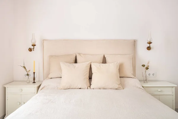 Lichte slaapkamer interieur, gezellig bed met beige linnen, droge bloemen op een nachtkastje. Retro en vintage stijl. Stockfoto
