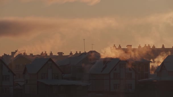 Kora reggel egy faluban. Téli naplemente füsttel a házak tetején, kéményekből..
