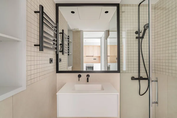 Μοντέρνος εσωτερικός σχεδιασμός του μπάνιου σε μπεζ με μαύρη μεταλλική διακόσμηση. Μπροστά όψη του μπάνιου με κουζίνα reglected στον καθρέφτη. — Φωτογραφία Αρχείου