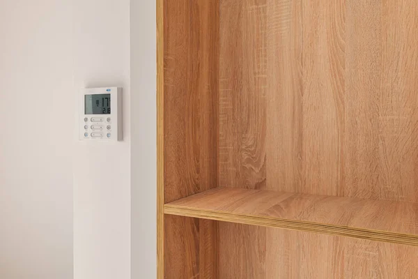 Climate control panel on the wall in a room with wooden built-in furniture with shelves