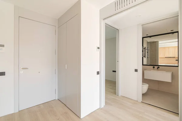 Entrance to the interior of modern apartment with white walls and wooden floor. View to the entrance door and bathroom with mirror. — Stock Photo, Image
