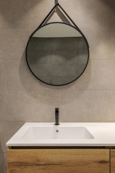 Μοντέρνο μπάνιο με λευκό νεροχύτη, ξύλινη βάση και στρογγυλό καθρέφτη. Minimalist στυλ εσωτερικού σχεδιασμού σε ζεστά χρώματα. — Φωτογραφία Αρχείου