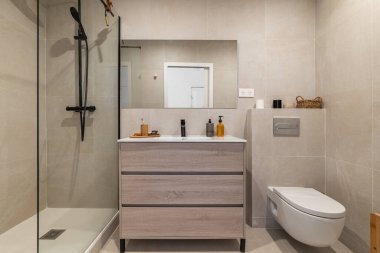 Cam duşlu modern banyo, ahşap kibir ve minimalist dekor. Tarafsız tonlar sakin bir atmosfer yaratır.