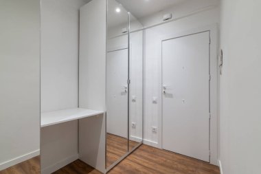 Geniş aynalı ve beyaz kapılı modern bir koridor. Zemin ahşap ve duvarlar beyaza boyanmış. Parlak ve ferah bir atmosfer yaratıyor..