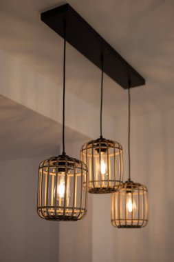 Kafes tasarımlı üç kolye lambası siyah bir tavan demirine asılmış. Işıklar, modern iç dekorasyonu geliştiren sıcak bir parıltı yayıyor..