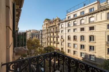 Klasik Barselona mimarisine bakan bir balkondan görüntü. Sahnede süslü binalar, açık mavi gökyüzü ve biraz yeşillik var..