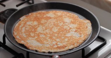 Gaz sobasında siyah bir tavada pişen altın sarısı krep. Krep pürüzsüz bir dokuya sahiptir ve eşit derecede pişirilir.