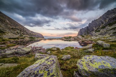 Gün batımında ön planda taşlarla dağ gölü 