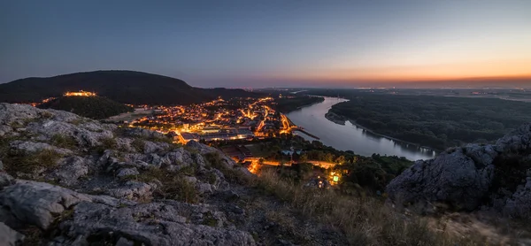 Upplysta små staden med floden från kullen vid solnedgången — Stockfoto