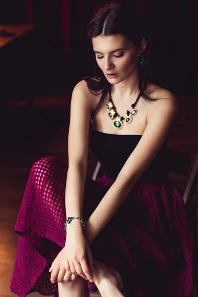 Woman in green jewelry sitting on chair looking down — Stock Photo, Image
