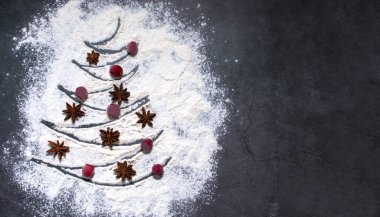 Christmas food background in the form of a Christmas tree painted on flour and a star-studded anise with frozen berries and a place for text.