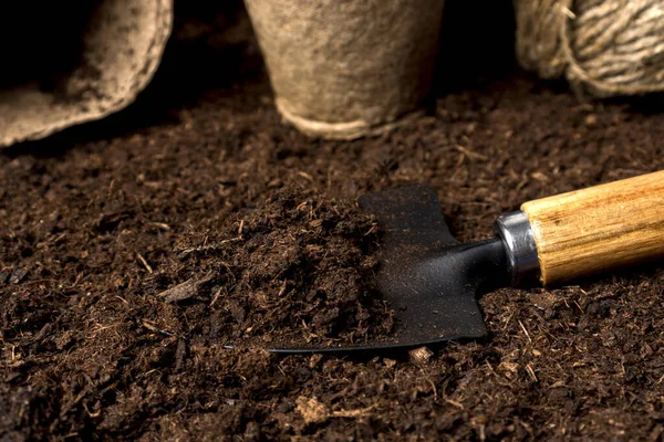 Fertile soil, peat on a garden shovel. The concept of natural agriculture, ecological cultivation of vegetables and fruits. Garden equipment and seedling tanks on the ground.