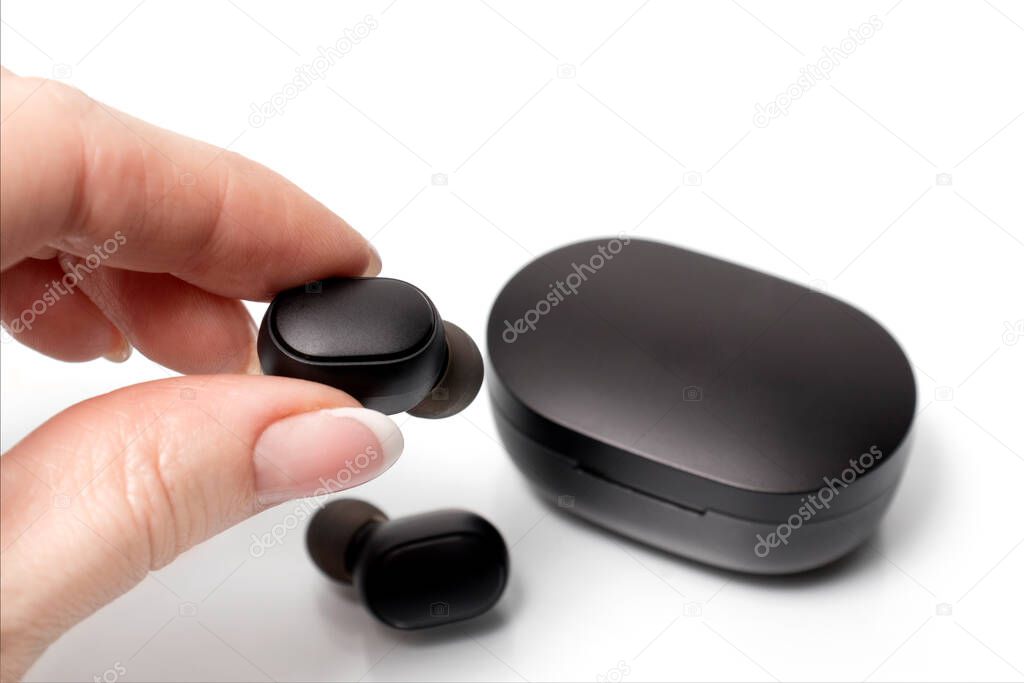 A woman's hand holds bluetooth in-ear headphones in a black color. Man wireless headphones
