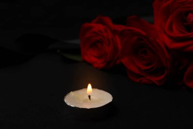 Burning mourning candle and red roses with black mourning ribbon on a dark background. The concept of grief, death, remembrance of the. selective soft focus.