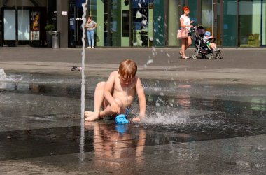 Bir çocuk, anormal sıcak bir havada, su damlacıklarıyla dışarıda bir çeşmede oynuyor. Anormal sıcaklık ve sıcak hava kavramı. Mogilev, Belarus - 21 Haziran 2021.