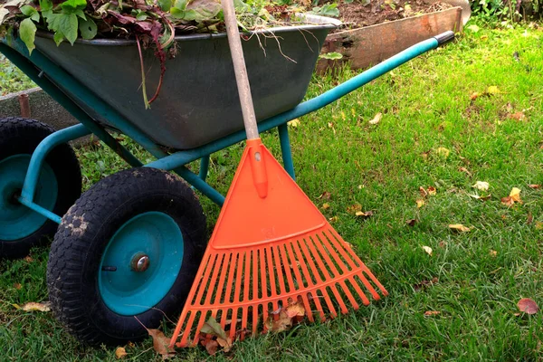 garden work. Garden rake and wheelbarrow in the garden. The concept of garden work on harvesting foliage, vegetable residues.